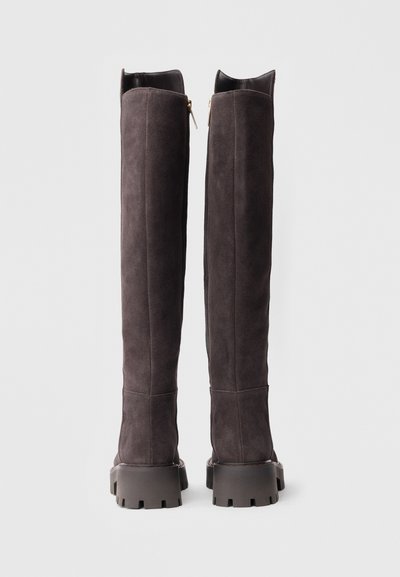 Bottes longues en daim gris foncé avec une semelle plate et épaisse. Dotées d'une fermeture éclair à l'arrière et de bords supérieurs structurés. Texture lisse.
