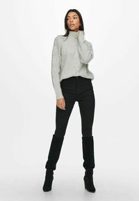 Light grey ribbed sweater with a high collar, button accent, paired with black skinny jeans and knee-high black suede boots.