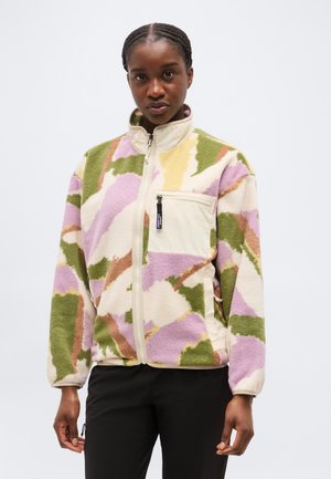 Žena oblečená v fleecovej bunde na zips s abstraktnými vzormi v zelenej, fialovej, béžovej a hnedej farbe a béžovým vreckom na hrudi so zipsom.