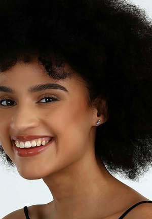 Silberne Steckerohrringe mit herzförmigem Design und klaren Edelsteinakzenten. Das Model hat lockige, dunkle Haare und einen neutralen Hintergrund.