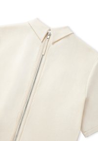 Krátký rukáv, krémová košile s zipem na zádech a límečkem typu polo. Hladká textura s čistými liniemi a minimalistickým designem.