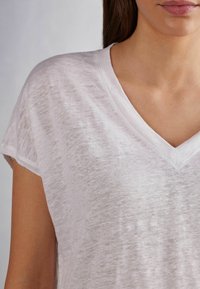 T-shirt bianco, leggero, con scollatura a V e maniche corte. Tessuto morbido e testurizzato con un aspetto leggermente trasparente. Design minimalista.