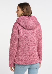 Rosa, strukturerad hoodie med huva och en logotypapplikation på vänster ärm. Har en figursydd design och mjukt material, kombinerad med ljusblå jeans.