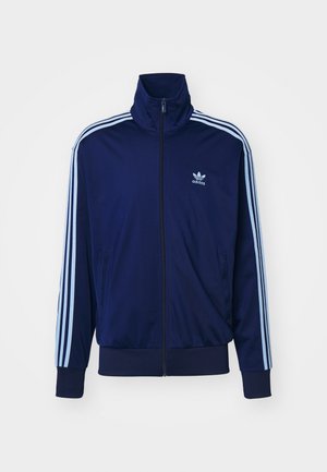Marineblaue Zip-Jacke aus glattem Stoff, mit drei hellblauen Streifen an den Ärmeln und einem kleinen Logo auf der Brust.