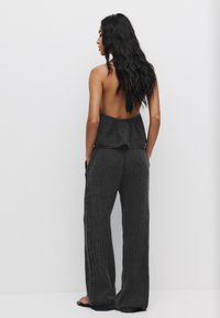 Ensemble deux pièces noir texturé avec un haut dos nu à volants. Pantalons larges et amples avec poches latérales.