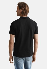 Fekete rövid ujjú galléros póló, sima anyagból készült; normál szabású, oldalán hasítékokkal a kényelem érdekében.