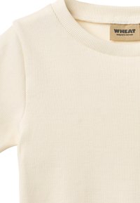 Chemise côtelée beige clair avec un col rond. Présente une texture douce et un motif subtil. L'étiquette indique « WHEAT conçu au Danemark ».