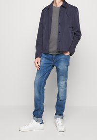 Chaqueta navy con cierre de botones sobre una camiseta gris, combinada con jeans de un tono azul claro y zapatillas blancas con acentos azules.