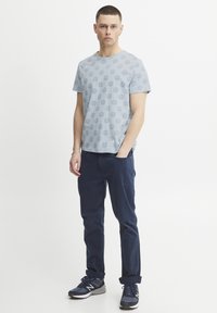 Lyseblå t-skjorte med sirkulært mønster, korte ermer, rund hals. Kombinert med marineblå bukser, modell med mørke joggesko.
