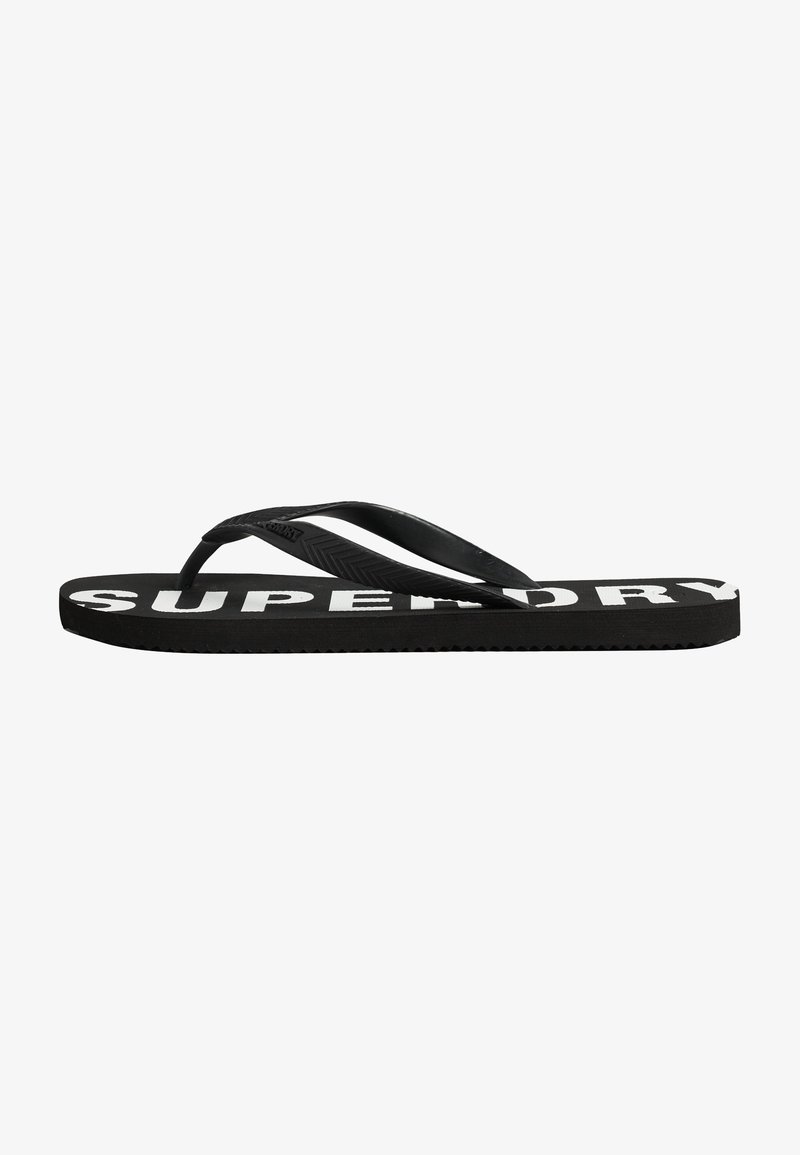 Tongs noires avec des brides en caoutchouc, dotées d'une semelle texturée et de "SUPERDRY" imprimé en blanc sur la semelle intérieure.