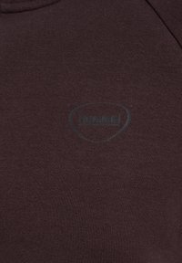 Dunkelbrauner Stoff mit einem dezenten schwarzen Hummel-Logo, das in der Mitte aufgedruckt ist.