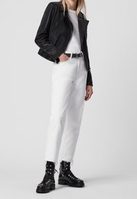 Svart skinnmotorcykeljacka, vit t-shirt, vita jeans och svarta snörkängor med grov sula, med fransig nederkant.