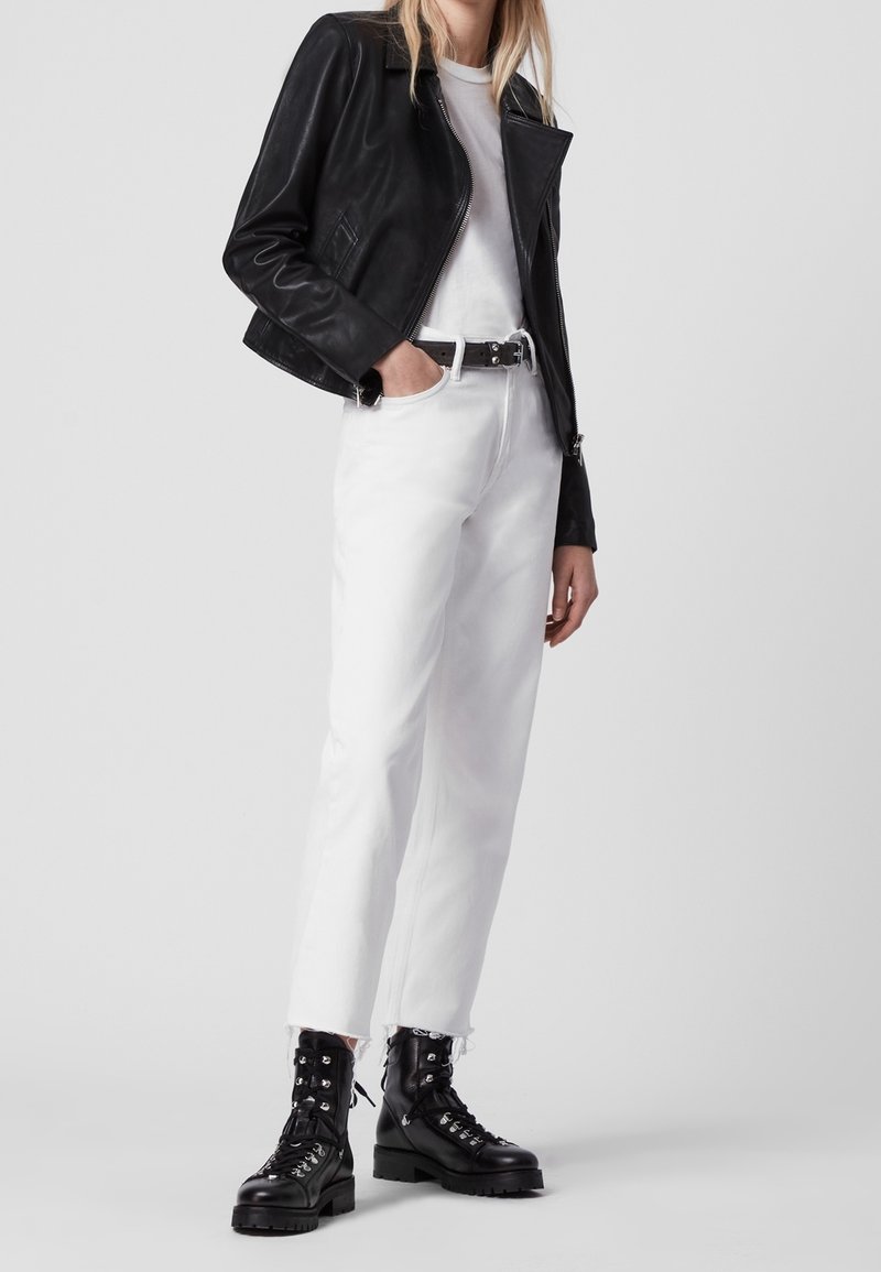 Svart skinnmotorcykeljacka, vit t-shirt, vita jeans och svarta snörkängor med grov sula, med fransig nederkant.