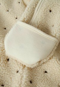 Tissu en polaire couleur crème avec de petits motifs en forme de losange foncés et gros plan sur une poche doublée d'un tissu lisse couleur beige clair.