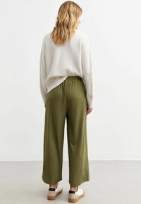 Pull beige à coupe ample avec des accents côtelés, associé à un pantalon plissé vert olive. La mannequin porte des baskets blanches avec des accents noirs.