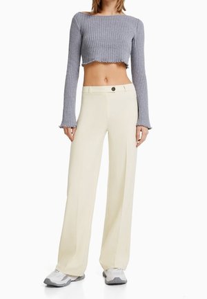 Haut à manches longues cropped côtelé gris associé à un pantalon large crème doté d'une fermeture à bouton, d'une texture lisse et d'un design ajusté.