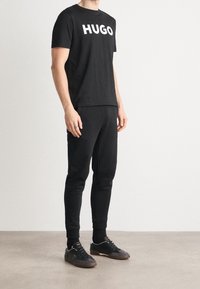 Camiseta de algodón negra con gran logo blanco "HUGO", combinada con joggers ajustados negros y zapatillas negras con detalles blancos.