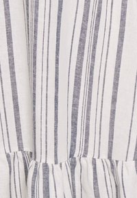 Vitt tyg med vertikala tunna och tjocka marinblå ränder samt en volangdetalj nära nederkanten.