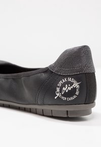 Black leather slip-on shoe with textured gray heel, featuring a circular logo in white, and a flexible rubber sole with ridges.