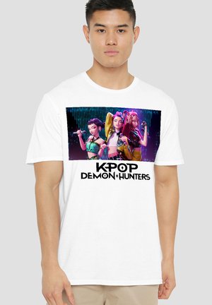 White t-shirt featuring a colorful graphic of three animated characters holding microphones, with "KPOP DEMON HUNTERS" text below.