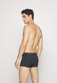 Schwarze Baumwoll-Boxershorts mit einem Logo-Bund, die eine enge Passform und eine glatte Textur aufweisen, von hinten mit einem neutralen Hintergrund gezeigt.