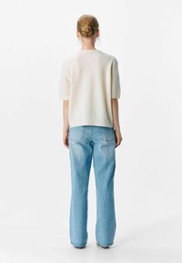 Elfenbeinfarbener kurzärmeliger Pullover mit gerippter Textur, kombiniert mit hellblauen, hochgeschnittenen Jeans. Einfaches, minimalistisches Design.