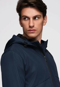 Námořnická voděodolná bunda s kapucí, se zipovým uzávěrem, nastavitelnými šňůrkami a dvěma bočními kapsami. Hladká, elegantní textura.