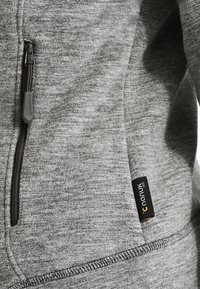 Zbliżenie na szary materiał polarowy z pionowym czarnym zamkiem błyskawicznym i małą czarną metką marki Nanuk 310.