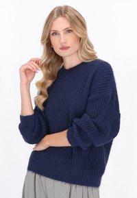 Granatowy sweter dzianinowy o prążkowanej fakturze, nieco luźny krój, okrągły dekolt i bufiaste rękawy, noszony na jasnoszarej spódnicy.