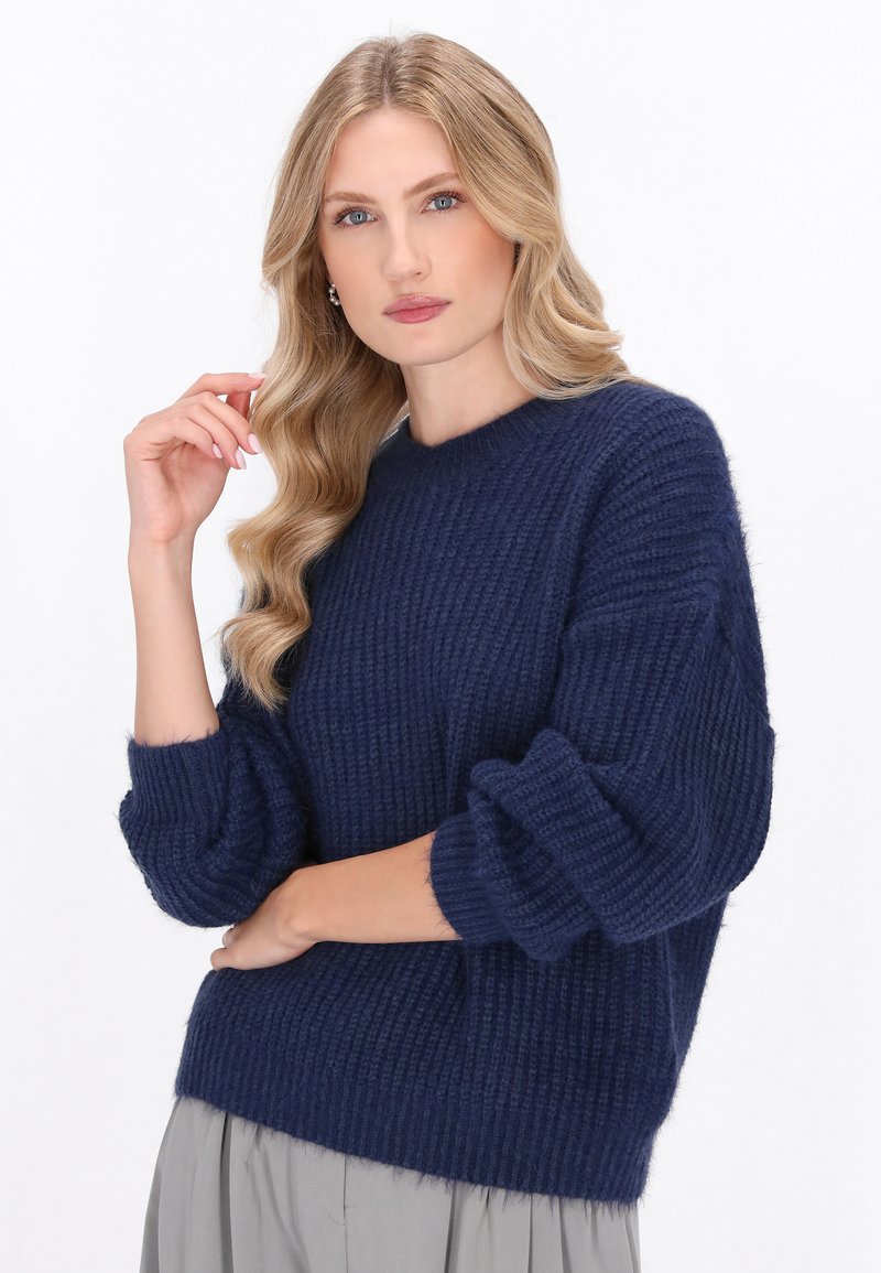 Granatowy sweter dzianinowy o prążkowanej fakturze, nieco luźny krój, okrągły dekolt i bufiaste rękawy, noszony na jasnoszarej spódnicy.