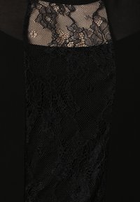 Musta kangas, jossa on herkkiä pitsipaneeleja monimutkaisilla kukkakuvioilla, kerrostettuna sileän, läpinäkymättömän materiaalin päälle. Täyteläiset ja läpikuultavat yksityiskohdat ovat ilmeisiä.