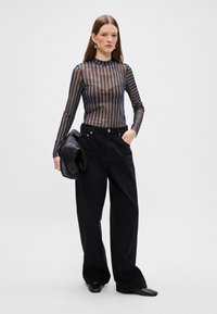 Pantaloni neri a vita alta con gamba larga abbinati a una blusa trasparente a maniche lunghe a righe. La blusa presenta righe verticali alternate in colori scuri.