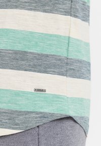 Striped skjorte i lysegrønt, marineblått og kremfarget; laget av myk stoff med en liten metallmerkelapp merket "ISOLID."