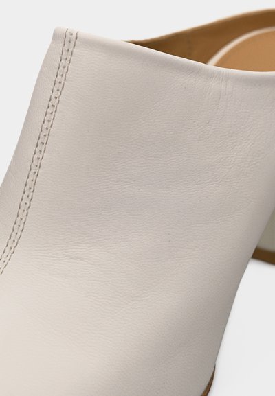 Κοντινή λήψη άνω μέρους λευκού δερμάτινου παπουτσιού που δείχνει ομαλή υφή και διπλή σειρά ραφής κοντά στην περιοχή της φτέρνας.