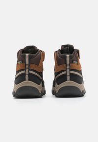 Braune und schwarze High-Top-Schuhe mit einer strukturierten Oberseite, verstärktem Absatz und Gummisohle mit tiefen Profilrillen. Wasserdichte Kennzeichnung an der Seite.