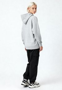 Felpa grigia con cappuccio, maniche lunghe, tasca a marsupio e polsini a coste, abbinata a pantaloni cargo neri e sneaker bianco e nero.