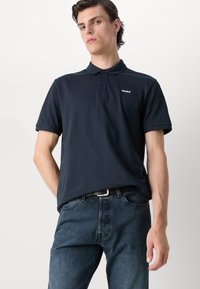 Tmavomodré polo tričko z bavlny, s klasickým golierom, zapínaním na tri gombíky a malým bielym logom na ľavej hrudi.