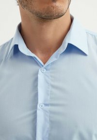 Chemise bleu clair avec une texture lisse, col pointu et deux boutons sur le plastron ; présente un design simple et classique.