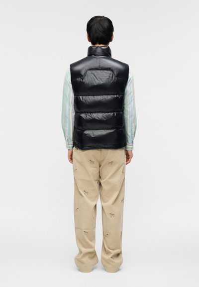 Tengerészkék pufi mellény magas gallérral és steppelt mintázattal, bézs kordnadrággal párosítva, amelyen apró, hímzett kutya minták találhatók.