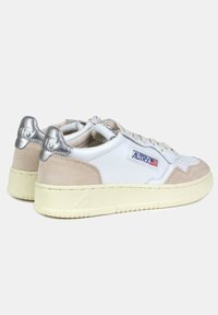 Sneakers bianchi in pelle con accenti in suede beige e linguette sul tallone in metallo argento. Presentano un design classico con lacci e una suola in gomma testurizzata.