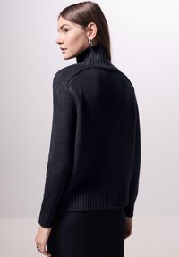 Schwarzer Strickpullover mit hohem geripptem Kragen, lockerer Passform sowie gerippten Bündchen und Saum. Minimalistisches Design, strukturierter Stoff.