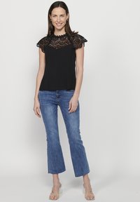 Zwarte blouse met kanten overlay op de schouders, gecombineerd met lichte spijkerbroek met flared pijpen en doorzichtige blokhakken. Eenvoudig en modern ontwerp.