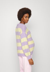 Sweater oversized em riscas púrpura pastel e amarelo, textura tricotada, punhos e bainha canelados, usado com calças rosa claro.
