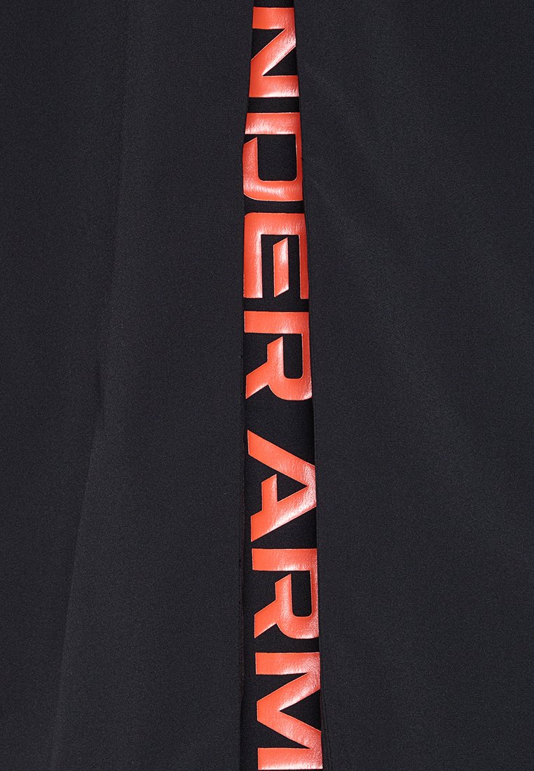 Un tissu noir présente une rayure verticale avec une inscription réfléchissante en orange "UNDER ARMOUR". La surface semble lisse et brillante.