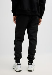 Pantalones jogger negros con acabado texturizado, cintura elástica y pierna cónica, combinados con zapatillas deportivas grises y blancas.