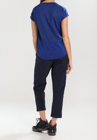 Sininen urheilupaita, jossa on lyhyet hihat, yhdistettynä tummansinisiin 3/4-pituisiin housuihin. Asusteena mustat ja liilat vaelluskengät.