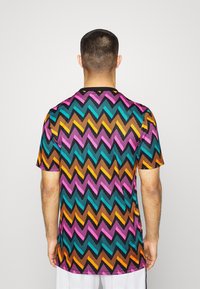 Kortärmad skjorta med ett flerfärgat zickzackmönster i rosa, teal, orange och brunt på en svart bakgrund, med en rund halsringning.