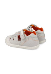 Zapatos de tela grises con acentos naranjas y una correa de velcro. Diseño abierto con una suela flexible y detalle del logotipo en el talón. Construcción ligera.