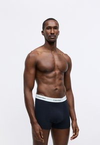 Calvin Klein black underwear with a white logoed waistband. The fabric is smooth, fitted, and has a classic boxer brief design.