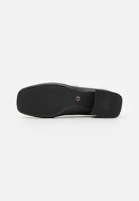 Black shoe sole with a smooth finish, featuring a textured pattern near the heel labeled "ANTI SLIDE" and a gold emblem in the center.